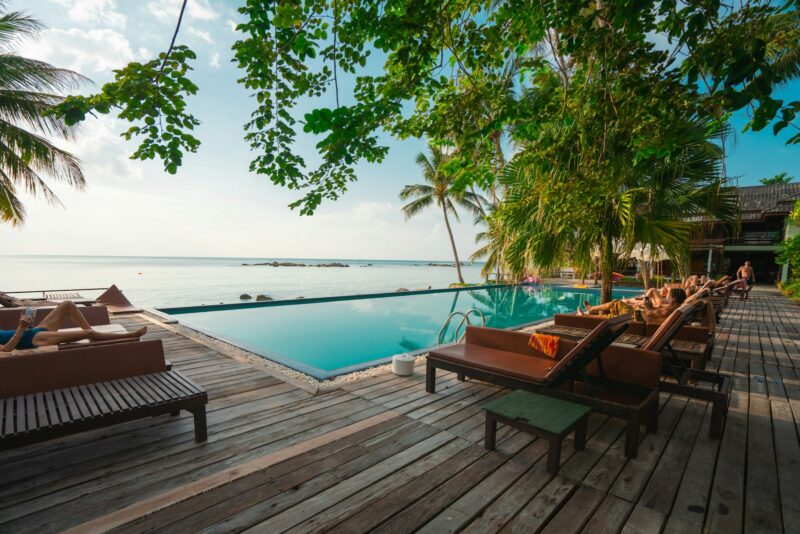 brown wooden table and chairs on brown wooden deck near body of water during daytime, white lotus resort
